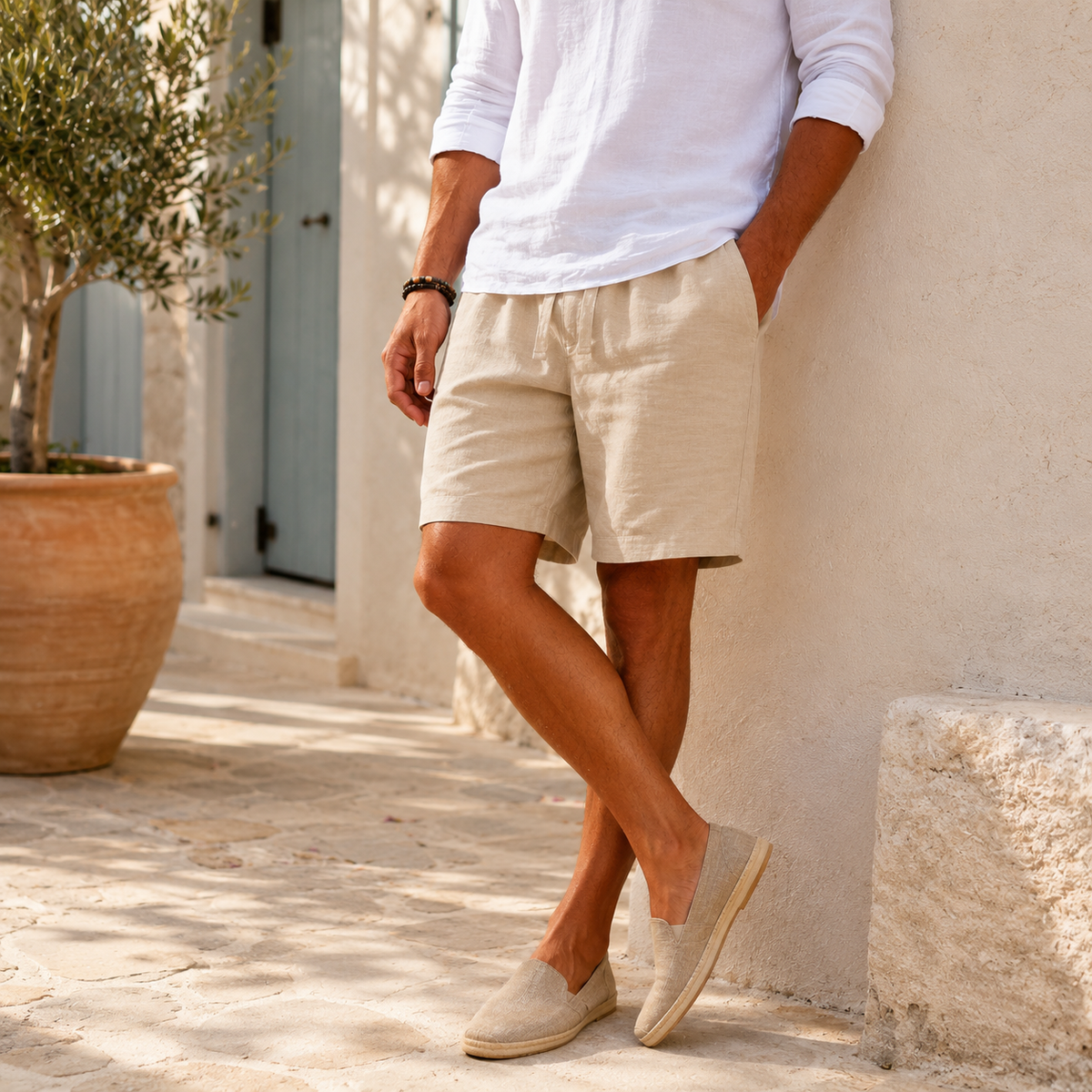 Model wearing men's beige linen drawstring shorts and espadrilles in Mediterranean setting - Rivaro
