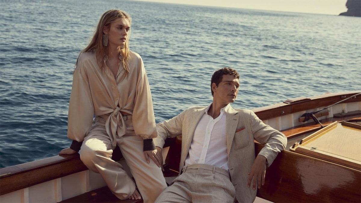 Couple wearing elegant neutral linen resort wear on a classic wooden boat in the Mediterranean sea - RIVARO Materials